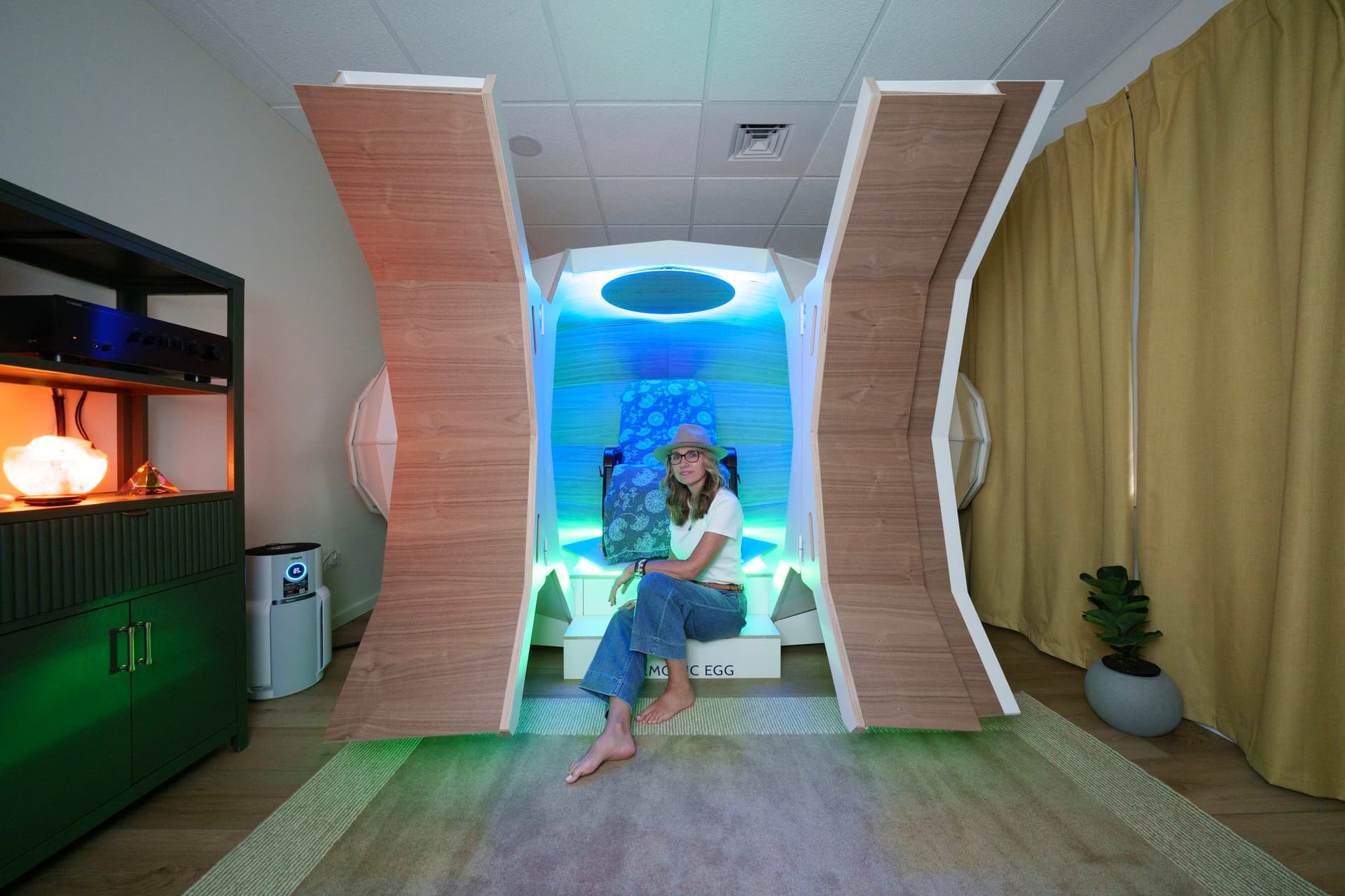 The Harmonic Egg chamber at Sparkle of Light Wellness — a smooth wooden egg-shaped room lit with soft colour, with a reclining chair inside.