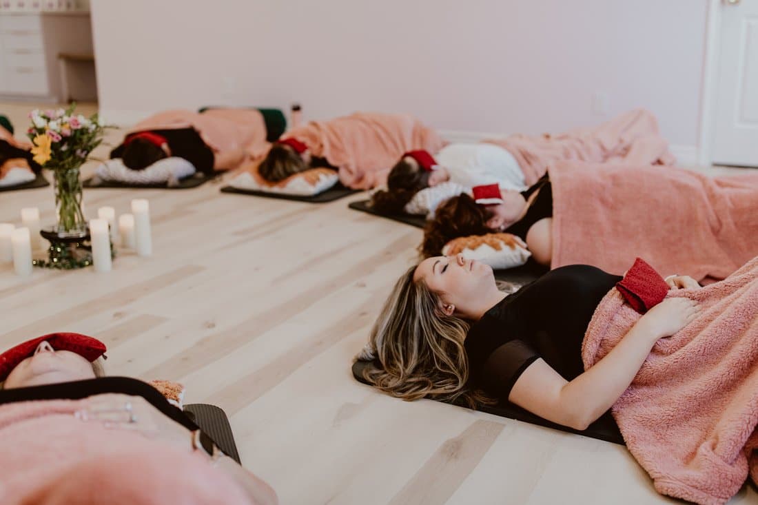 People resting on mats in a candlelit room during a guided group relaxation session.