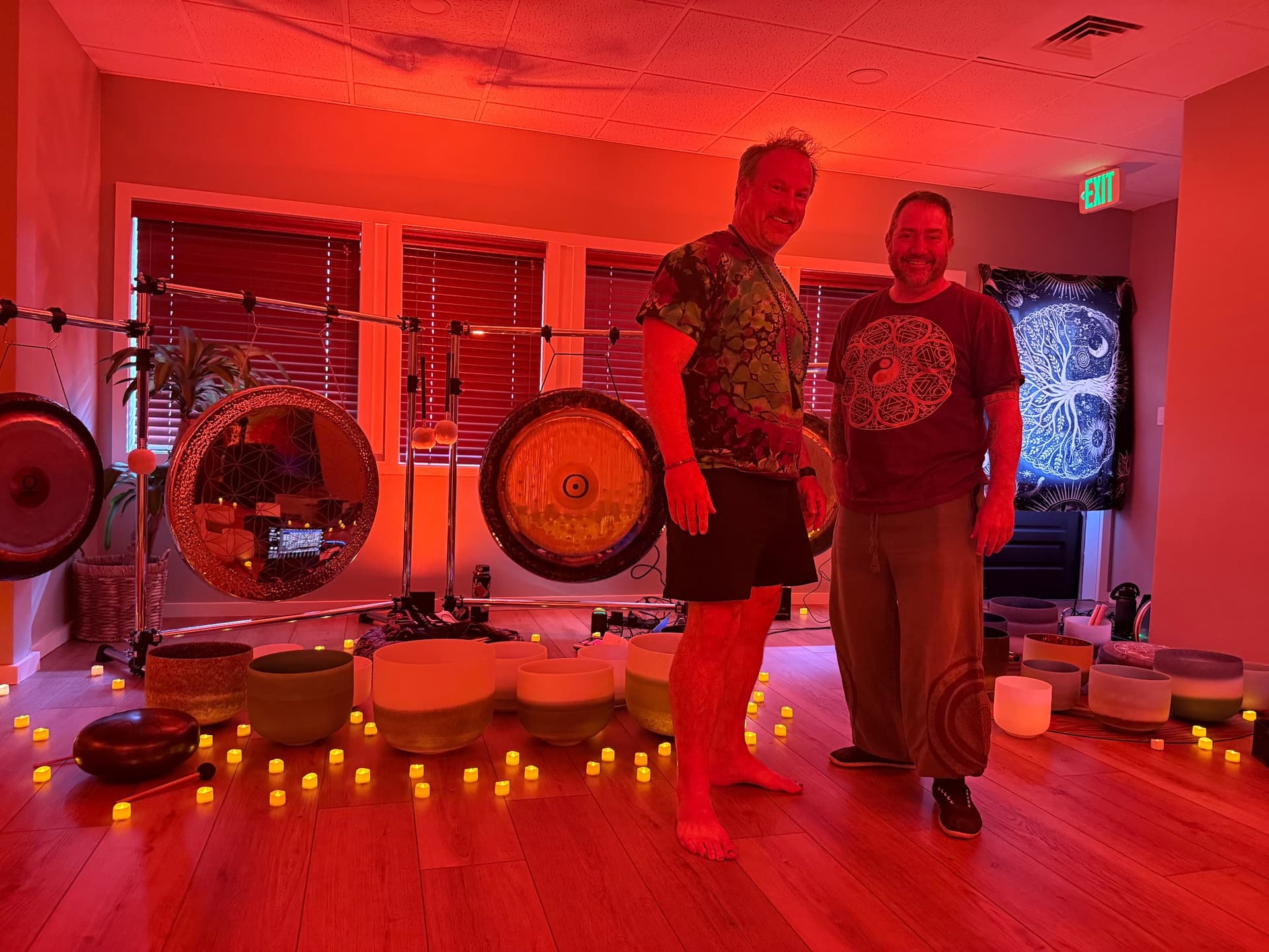 Jon Demel seated outdoors in white clothing, playing a set of crystal singing bowls.